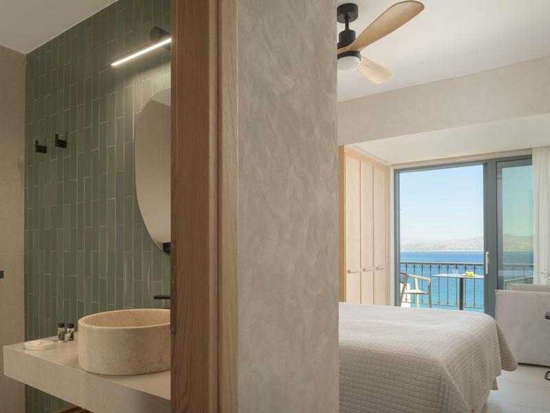 Lichte hotelkamer met zeezicht en badkamer met ronde wastafel.