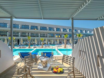 Moderner Außenbereich mit Holzstühlen, Tisch, Pool und mehrstöckigem Hotel im Hintergrund.