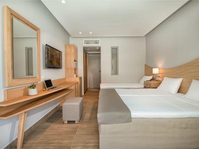 Hotelzimmer mit zwei Betten, Holzmöbeln, grauen Wänden und warmem Deckenlicht.