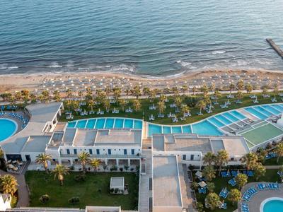 Strandhotel mit mehreren blauen Pools, grünem Garten und Holzsteg am Sandstrand.
