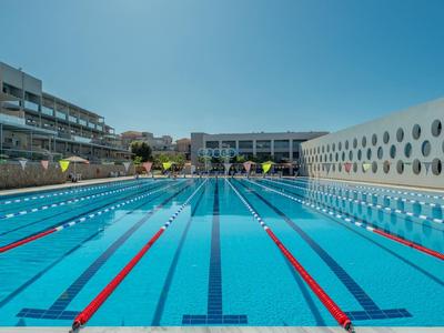 Außen-Schwimmbecken mit Bahnen, blauem Wasser, klarer Spiegelung und umliegenden Gebäuden.