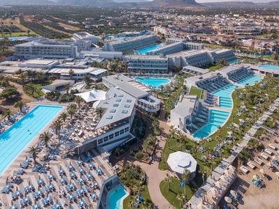 Große Urlaubsanlage mit mehreren blauen Pools, Sonnenliegen und Gebäuden in sonniger Landschaft.