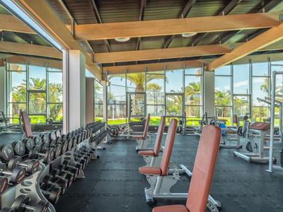Großer, heller Fitnessraum mit Hanteln, Trainingsgeräten und großen Fenstern zur Außenansicht.