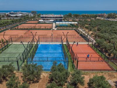 Mehrere Tennisplätze mit rotem und blauem Boden, von Bäumen und Zäunen umgeben, am Meer gelegen.