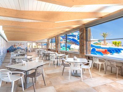 Freier, überdachter Außenbereich mit Tischen und Stühlen neben einem Hotelpool bei Sonnenschein.