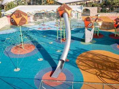 Bunter Kinderspielplatz mit Wasserspielen und Rutschen auf blauem Bodenbelag neben Pool.
