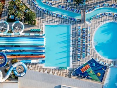 Großer Hotelpool mit runden und rechteckigen Becken, Liegestühlen und Wasserrutschen, Luftaufnahme.