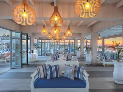 Open hotel lounge area with blue cushions, stylish lamps, and glass windows overlooking the sunset.