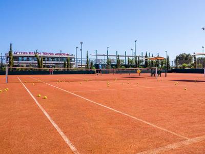Red clay tennis court under a clear blue sky with net and fencing.