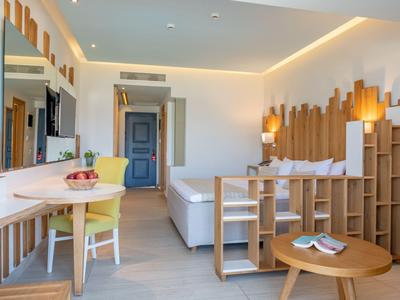 Helles Hotelzimmer mit Holzmöbeln, Sofa, Schreibtisch und warmem Licht.