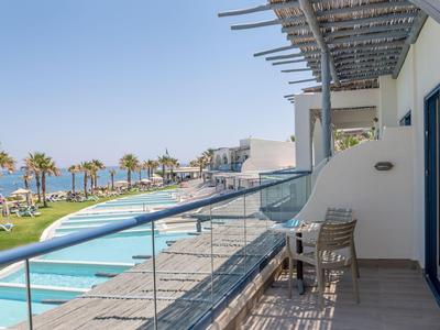 Balkon mit Stühlen und Blick auf Pool, Strand und Meer bei klarem Himmel im Hotel.