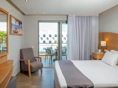 Helles Hotelzimmer mit bequemem Doppelbett, Sessel, Schreibtisch und Balkon mit Blick nach draußen.