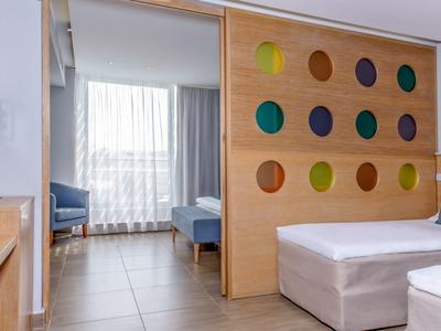 Modernes Hotelzimmer mit Doppelbett, bunter Wanddekoration und Sitzbereich mit Sofa.
