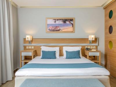 Modernes Hotelzimmer mit Doppelbett, blauem Bettzeug, Nachttischen und maritime Wanddekoration.