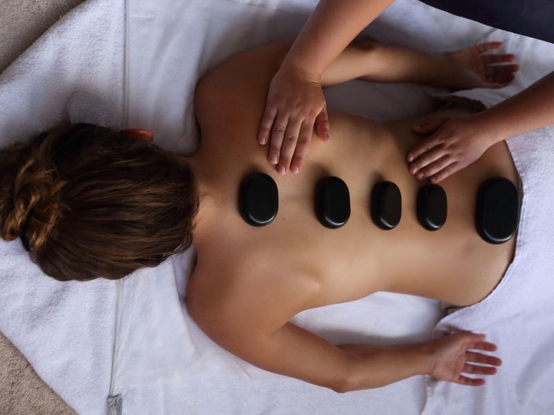 Person receives hot stone massage lying on a towel, spa treatment for relaxation and wellness.
