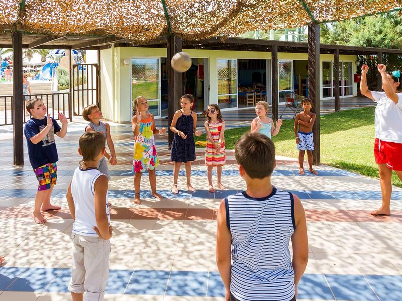 Group of children playing a game outside under shade near a building.