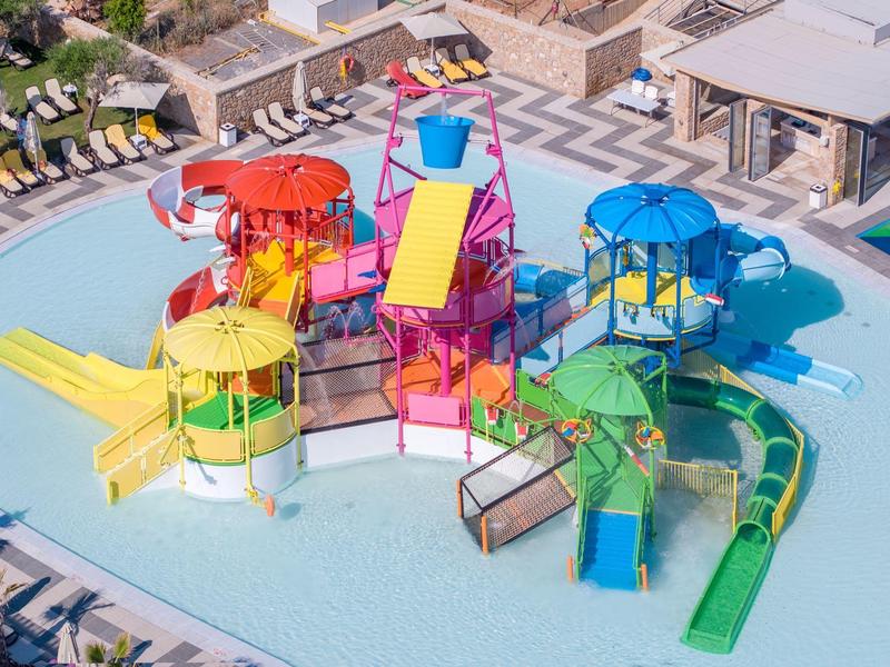 Colorful water play structure with slides in a shallow pool at a resort outdoor area.