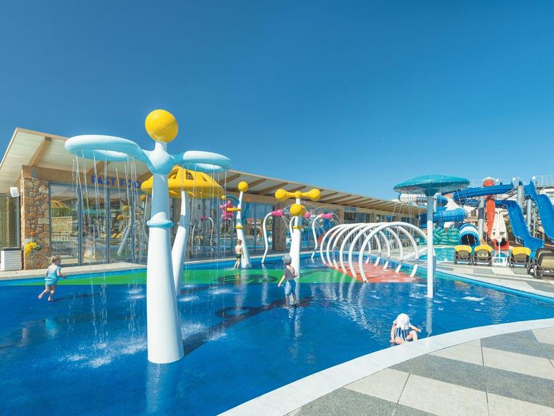 Outdoor water play area with fountains, slides, and splash features under a clear blue sky.