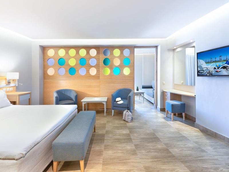 Modern hotel room with large bed, colorful wall decor, seating area, and flat-screen TV.