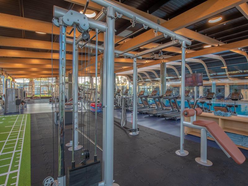 Spacious hotel gym with various exercise machines and a running track under wooden ceiling beams.