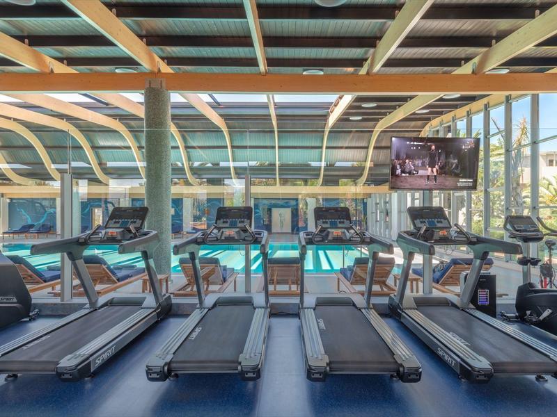 Hotel gym with treadmills and exercise bikes facing large windows and a pool outside.