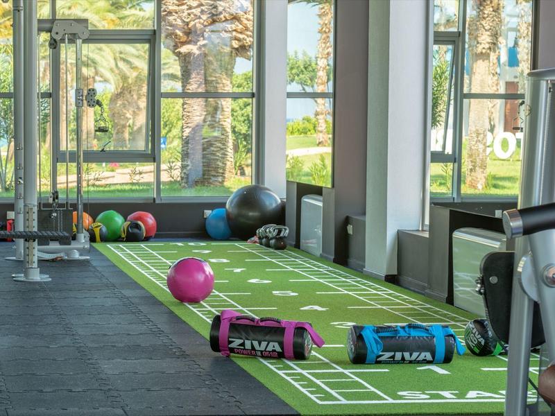 Gym room with exercise mats, colorful weights, and large windows overlooking a green garden.