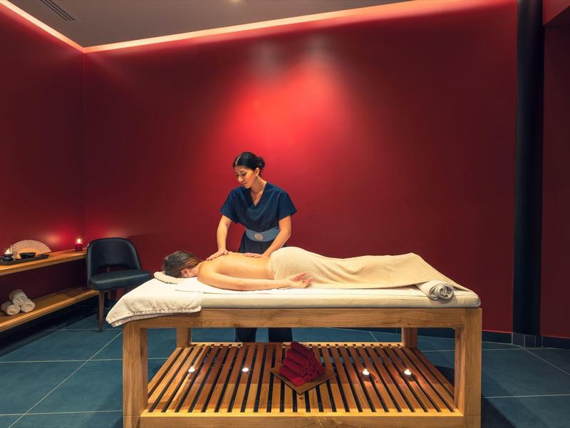 Massage therapist giving a back massage in a cozy, dimly lit red room at a spa.