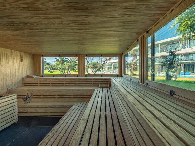 Wood-paneled sauna with tiered wooden benches and large windows overlooking outdoor greenery.