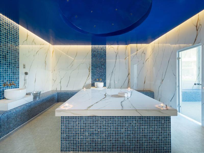 Modern spa room with blue mosaic tiles, marble walls, and ambient LED lighting.