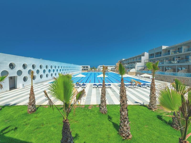 Modern hotel pool with sun loungers, green palm trees, and clear blue sky.
