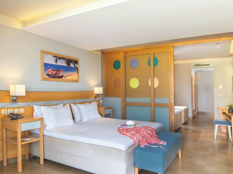 Modern hotel room with large bed, wooden partition, and purple ottoman