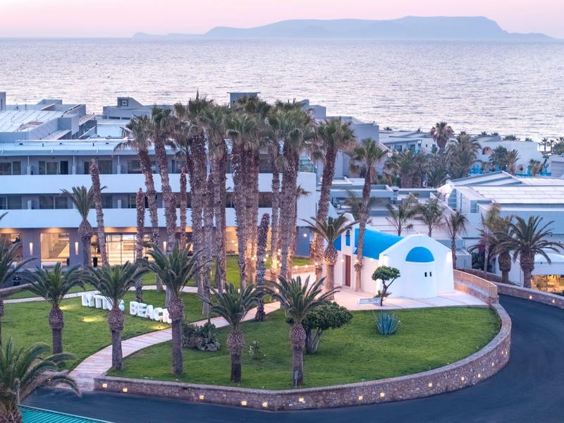 Resort with palm trees, a pool, and sea view at sunset with distant mountains.