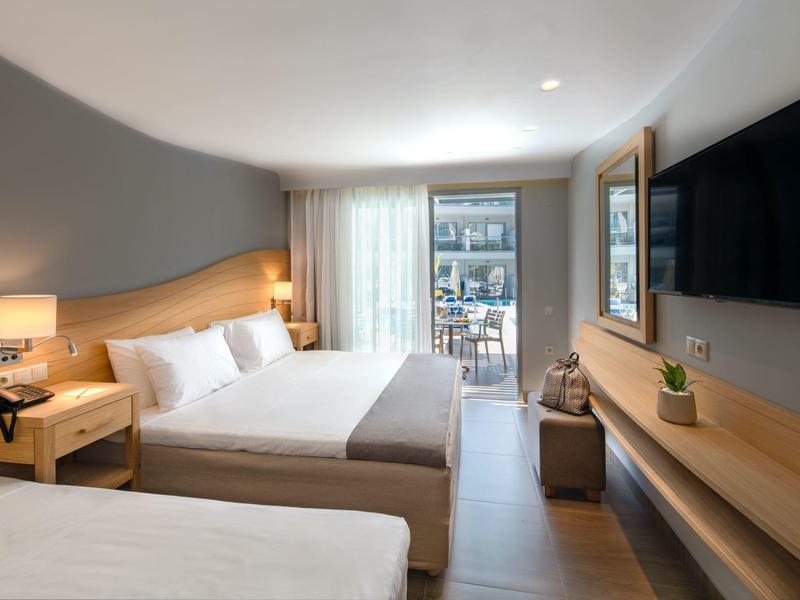 Modern hotel room with two beds, wooden furniture, and a balcony with city view.