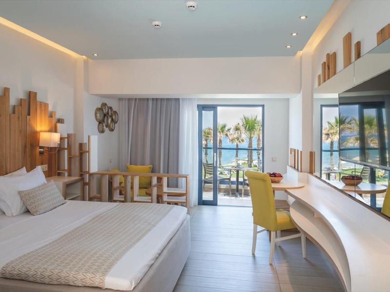 Modern hotel room with king-size bed, yellow chair, and view of pool and palm trees.