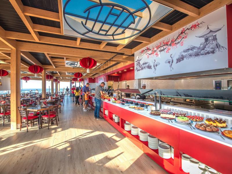 Bright restaurant interior with red accents, buffet area, and wooden ceiling beams.