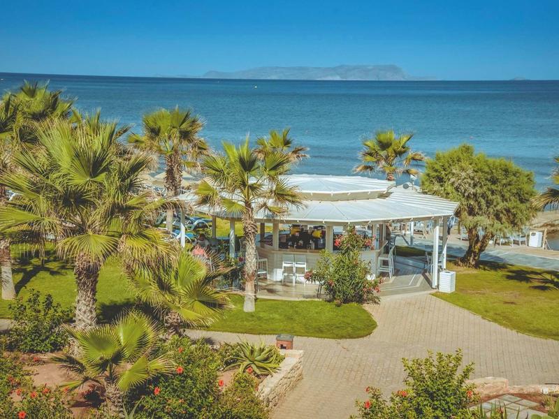 Round seaside restaurant surrounded by palm trees and blue sky.