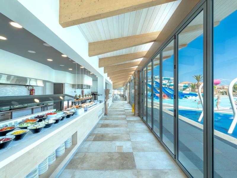 Outdoor buffet area with expansive glass windows overlooking a swimming pool and clear blue sky.