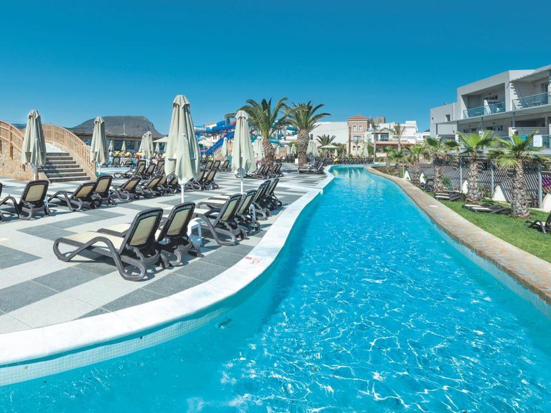 Long hotel pool with sun loungers and modern hotel buildings in the background.