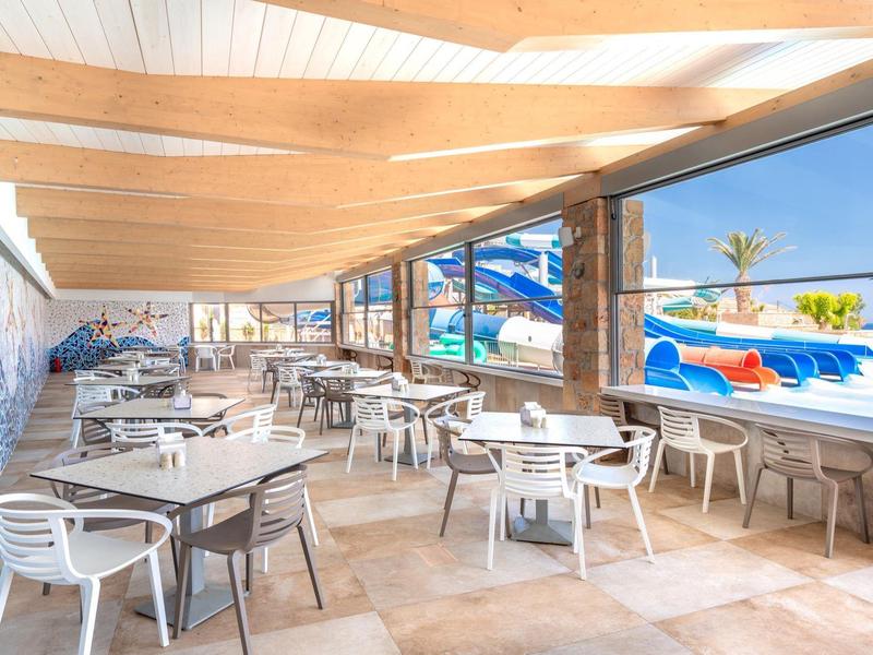 Bright covered outdoor restaurant with white tables and chairs next to pool and water slides.