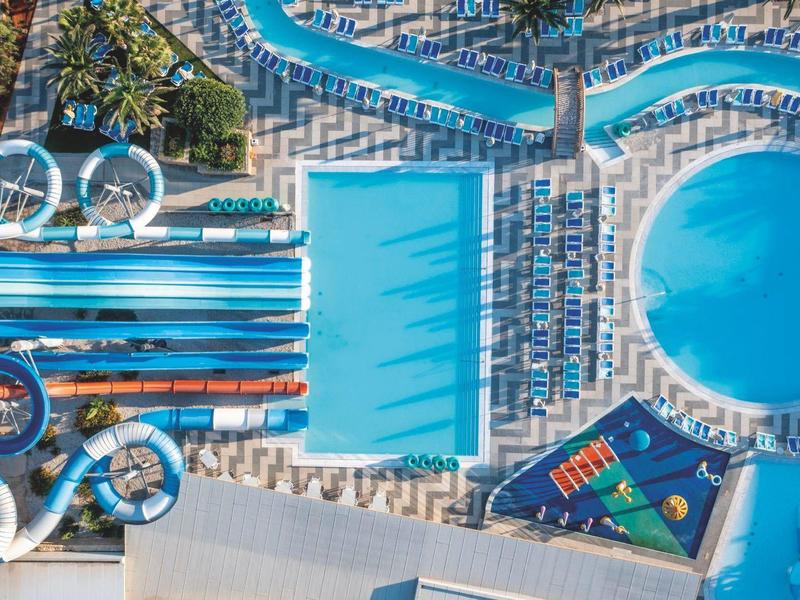 Aerial view of a pool with colorful loungers and water slides at a hotel resort.