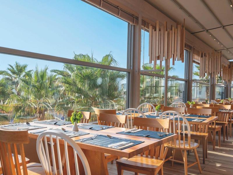 Brightly furnished restaurant with large windows and palm tree views.
