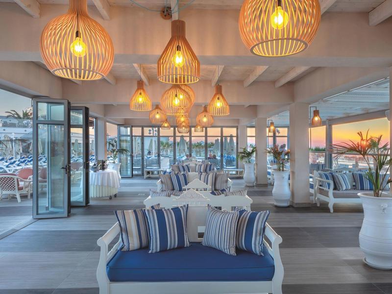 Open hotel lounge area with blue cushions, stylish lamps, and glass windows overlooking the sunset.