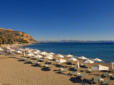 Spiaggia sabbiosa con file di ombrelloni bianchi e mare blu calmo sotto un cielo limpido