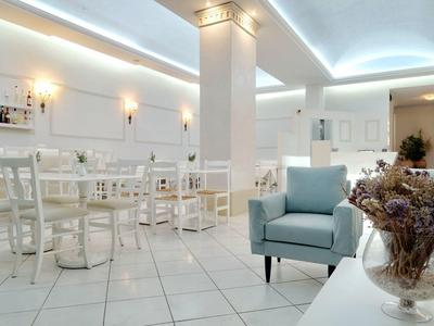 Caffetteria luminosa e moderna con mobili bianchi, poltrona blu e fiori secchi sul tavolo.