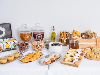 Buffet con vari tipi di pane, biscotti, salumi, bevande e dolci su un tavolo bianco.