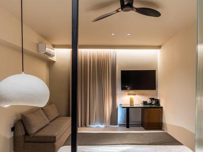 Camera d'hotel moderna con divano, TV, ventilatore a soffitto e luce calda.