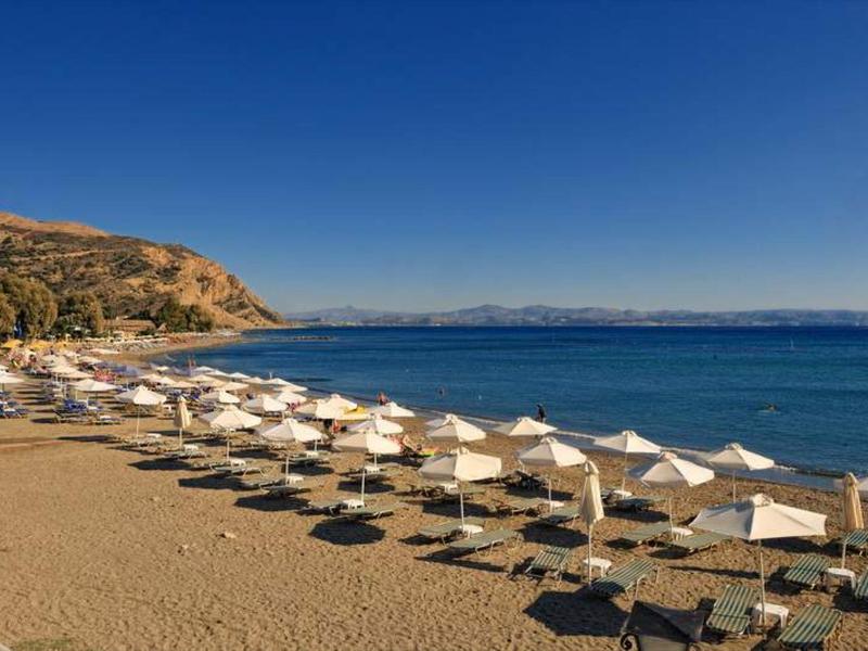 Spiaggia sabbiosa con file di ombrelloni bianchi e mare blu calmo sotto un cielo limpido