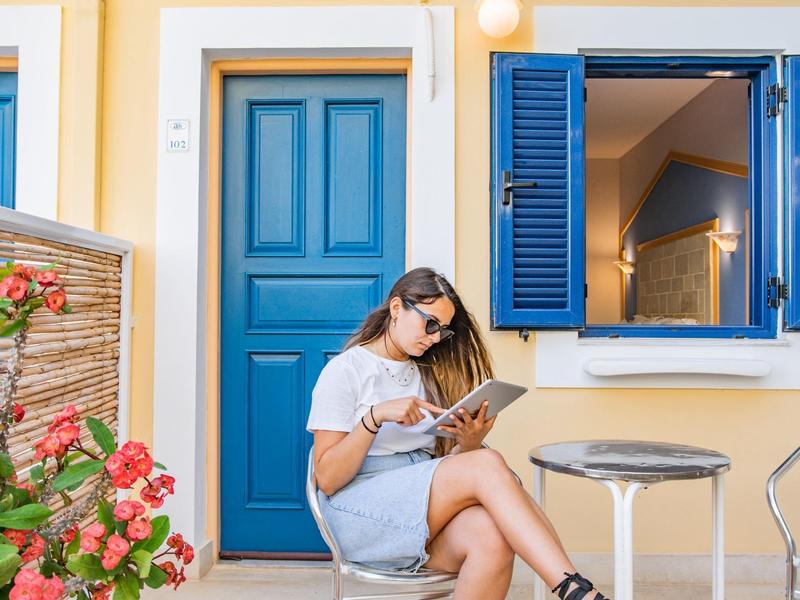 Donna che legge un libro accanto a una porta e una finestra blu vicino a piante in fiore.