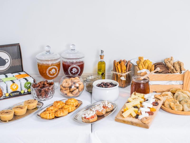 Buffet con vari tipi di pane, biscotti, salumi, bevande e dolci su un tavolo bianco.