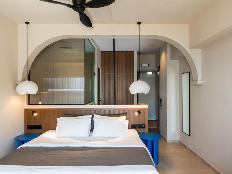 Camera moderna con letto matrimoniale, dettagli in legno e due lampade sospese sotto un arco.